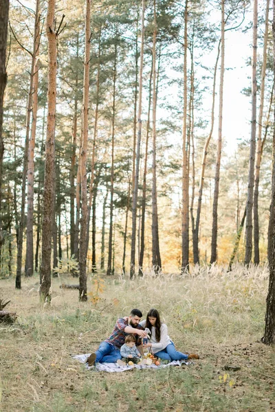 Estilo de vida ao ar livre retrato de família de pais jovens com filho pequeno, se divertindo juntos, enquanto sentado no cobertor na bela floresta de outono no dia ensolarado — Fotografia de Stock