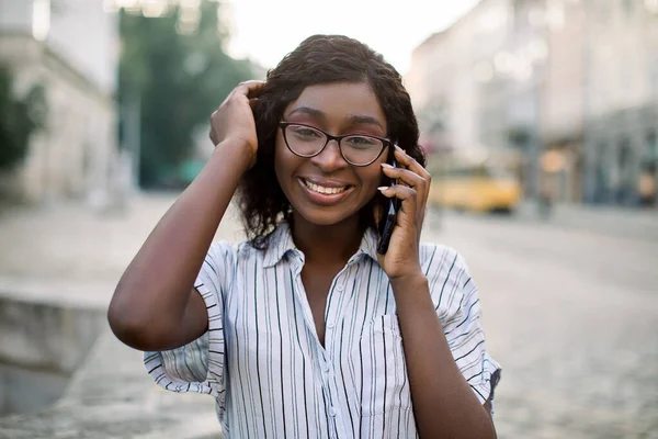 Close-up portret van een glimlachende Afrikaanse vrouw in een bril, wandelen in de oude stad met een mobiele telefoon, praten met haar vriend en glimlachen naar de camera. Begrip "mens, ras en technologie" — Stockfoto