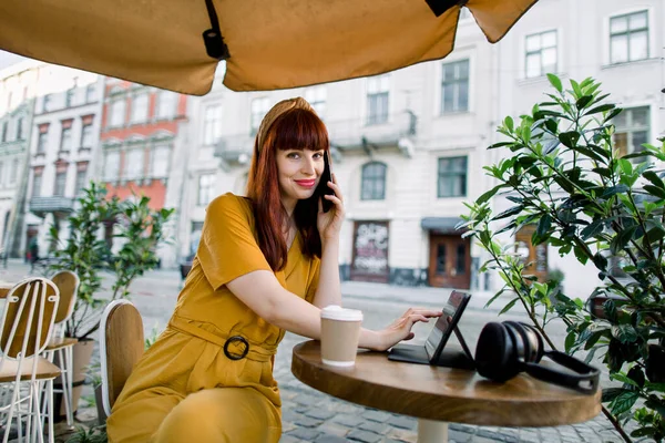 Miejski styl życia, przerwa na kawę na świeżym powietrzu. Ładnie uśmiechnięta rudowłosa kobieta biznesu w żółtych stylowych ubraniach, za pomocą tabletu na przerwę obiadową siedzi przy stole w parku kawiarni miejskiej — Zdjęcie stockowe