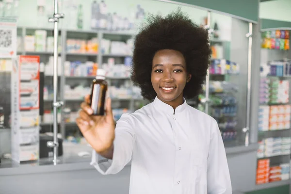 Sebevědomá usmívající se africká žena, lékař nebo lékárník pózující nad nemocničním lékárenským zázemím, držící lahvičku léku v rukou. Zaměření na obličej — Stock fotografie