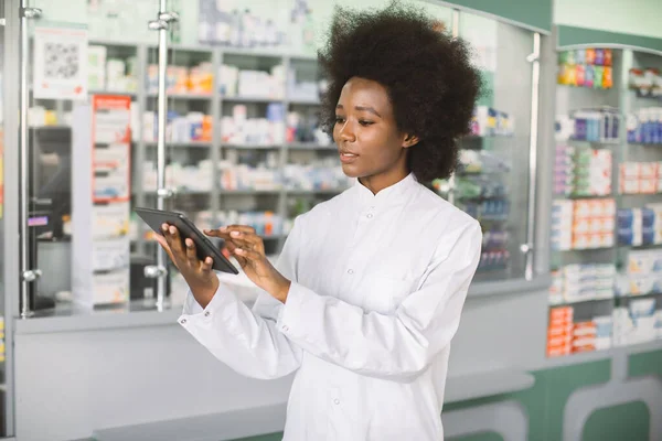 젊고 자신감 있는 젊은 아프리카 여성 의사나 약사가 현대의 병원 약국이나 진료소 내부에서 서 디지털 태블릿을 사용하는 모습을 클로즈업 사진 — 스톡 사진