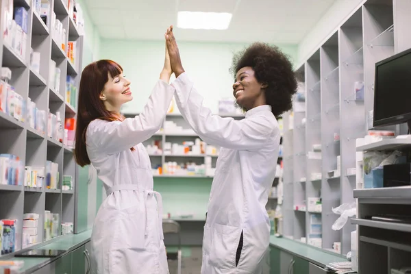 두 명의 행복 한 여성 colleages 약사, 아프리카와 코카서스 여성 약국에서 일하는, 웃는, 5 제공, 서로를 찾고 재미를 즐기고. — 스톡 사진