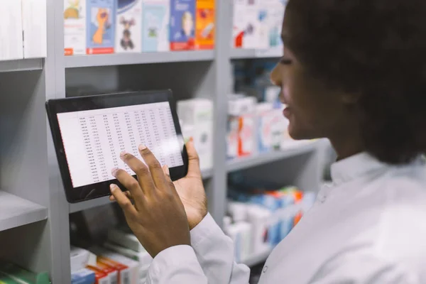 현대적 인 병원 약국 내부에 서 있는 동안 디지털 태블릿을 사용하여 마약 품질 관리를 하는 아프리카계 미국인 여성 의사나 임상 약사의 근접 촬영 — 스톡 사진