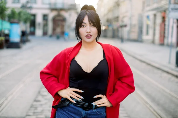 Hezká asijská žena s černými copánky, oblečená do stylové neformální červené bundy, černé tílko a džíny, stojící na městské silnici a sexy dívající se do kamery. Urban fashion, lifestyle concept — Stock fotografie