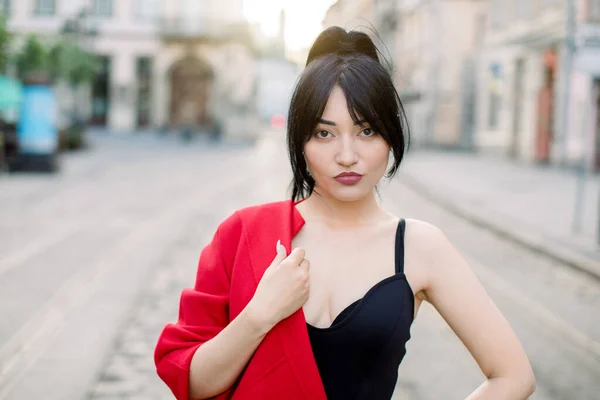 Retrato de rua de jovem sexy bela mulher asiática, vestindo elegante top preto elegante e blazer vermelho em um ombro, olhando para a câmera. Conceito de moda feminina. Espaço de cópia — Fotografia de Stock