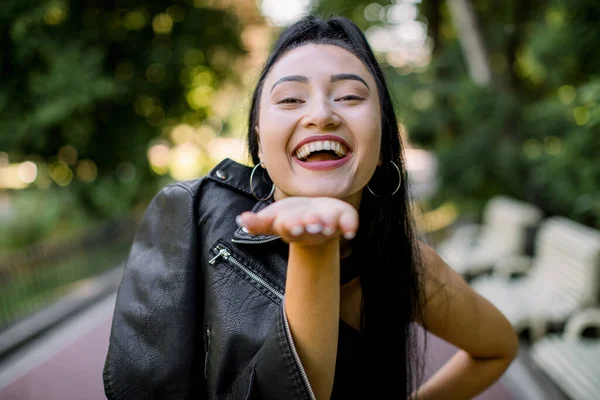 Tersenyum ceria bahagia wanita Asia, mengenakan jaket kulit hitam, berdiri di luar ruangan atas latar belakang taman alam. Menutup potret gaya hidup di luar ruangan. Orang, ras, konsep emosi — Stok Foto