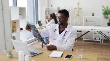 Doktor, sağlık hizmetleri, tıbbi teknoloji ve uzmanlık alanlarında röntgen analizi yapıyor. Görüntü, 30 yaşlarında Afrika kökenli yetişkin bir erkeğin çalışma alanında profesyonel giysiler giydiğini gösteriyor.