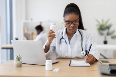 Steteskop kullanan, ilaç yazan, reçete yazan, dizüstü bilgisayar kullanan beyaz önlüklü kadın bir doktor. Çalışma alanı, sağlık hizmetleri ve odaklanmayı öneren saksı fabrikası, telefon ve ilaç araçlarını içerir..