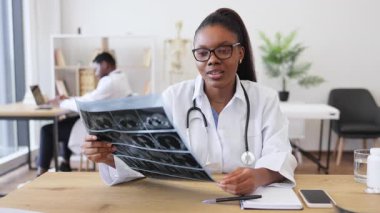 Genç bir kadın doktor klinik ortamdaki radyografik görüntüleri analiz ediyor, profesyonellik gösteriyor. Olay yeri, sağlık hizmetlerinde tıbbi uzmanlık, teknoloji kullanımı ve hasta bakımını betimliyor