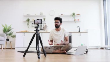 Genç yetişkin bir adam meditasyon yapıyor, huzurlu mutfak ortamında sağIık videosu kaydediyor. Çevrimiçi öğretim için sağlıklı yaşam tarzı, farkındalık egzersizi ve içerik oluşturmayı teşvik eder