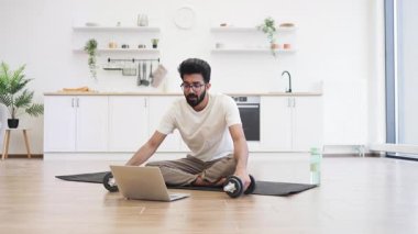 Paspasın üzerinde oturan genç adam dambıllarla egzersiz yapıyor, sağlık video blogunu içeride kaydediyor. Sahne fitness, teknoloji ve ev rutini kavramını öneriyor..