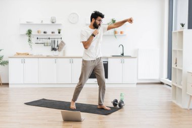 30 'lu yaşlardaki adam yoga minderinin üzerinde geniş mutfakta boks egzersizleri yapıyor..