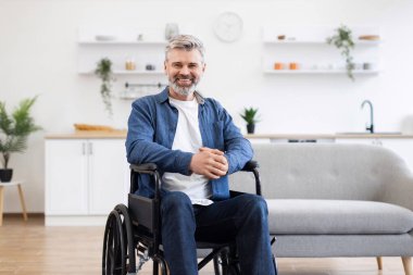 Günümüz oturma odasında, parlak iç dekorasyonlu, bağımsızlığı ve pozitifliği temsil eden, gündelik kıyafetli, gülümseyen olgun bir adamın portresi. Model orta yaşlı beyaz bir erkek.