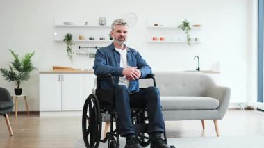Gri saçlı bir adam, parlak oturma odasında, tekerlekli sandalyede oturuyor.