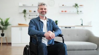 Günümüz oturma odasında, parlak iç dekorasyonlu, bağımsızlığı ve pozitifliği temsil eden, gündelik kıyafetli, gülümseyen olgun bir adamın portresi. Model orta yaşlı beyaz bir erkek.