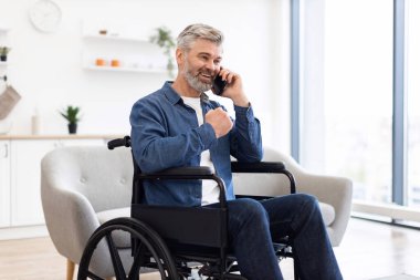 Tekerlekli sandalyede oturan, cep telefonuyla gülümseyen olgun bir beyaz adam. Sahne, iletişim, bağımsızlık, pozitiflik ve çağdaş yaşam tarzını betimliyor.