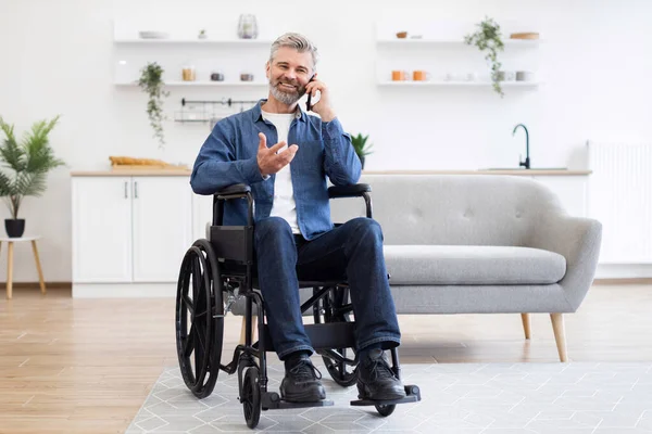 Tekerlekli sandalyede oturan olgun beyaz adam ev ortamında cep telefonuyla konuşuyor. Gündelik yaşam anı parlak ve modern bir iç dekorla sunuluyor..