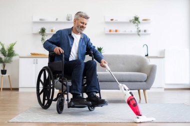 Elektrikli süpürge tutan orta yaşlı bir adam, ev temizliği faaliyetlerine katılıyor, modern oda düzenliyor.