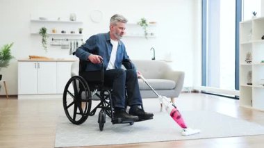 Elektrikli süpürge tutan orta yaşlı bir adam, ev temizliği faaliyetlerine katılıyor, modern oda düzenliyor.