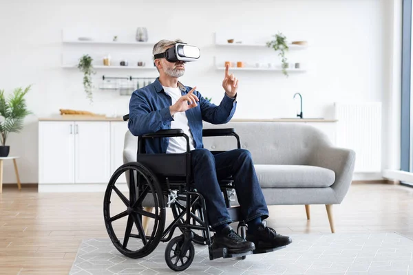 Tekerlekli sandalyedeki yaşlı adam sanal gerçekliği VR kulaklıkla yaşıyor. Modern, parlak bir iç mekan ortamında fiziksel jest temelli etkileşime giriyor..