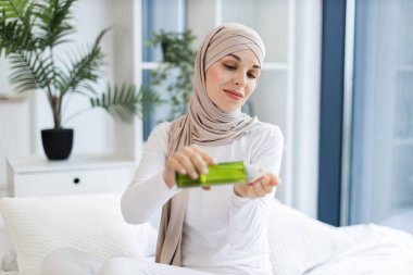 Başörtüsü takan genç Müslüman kadın el kremi sürüyor, içeride rutin cilt bakımını yapıyor..