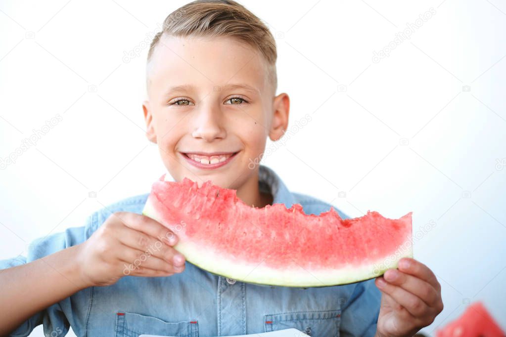 Happy boy is eating watermelon and smiling at the white background