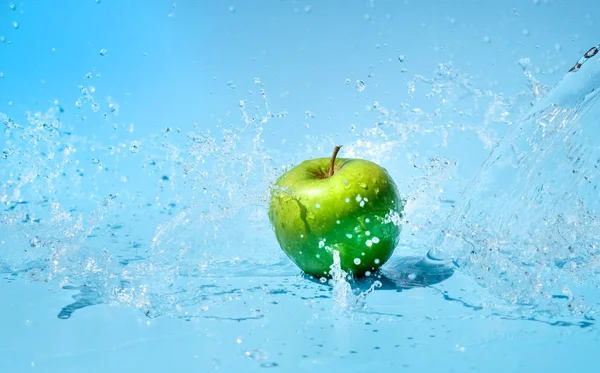 Green apples in clear water splash on blue background