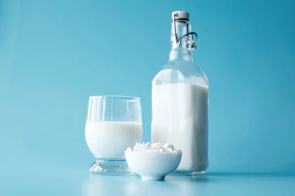 Bottle of milk, glass of milk, cottage cheese in white round bowl at blue background