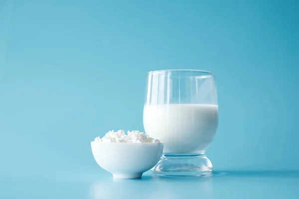 Bottle of milk, glass of milk, cottage cheese in white round bowl at blue background