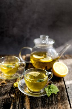 Güneşli gün ışığında cam bardak ve çaydanlık limon ve bal ile bitkisel çay