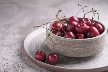 Kırsal seramik tabakta ahşap zeminde su damlaları olan kırmızı kiraz meyvesi.