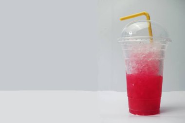 Beyaz masadaki plastik bardakta buzlu meşrubat. Kırmızı su, limonlu soda, berrak plastik bardaktaki buz içme suyu, yaz teknisyenlerindeki susuzluğu ve tazeliği gidermeye yardımcı oluyor. Beyaz zemini yerleştir. Seçmeli odak