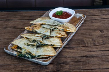 Tortilla, ıspanak ve peynirli tortilla çıtır çıtır, ahşap bir tabakta domates sosuyla servis edilir. Seçimli ve bulanık bir odak noktası..