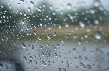 Arabanın cam yüzeyine bulutlu bir arka plan ile yağmur damlası düşer. Doğal desen. Yağmurdan sonra bardağa su damlıyor.