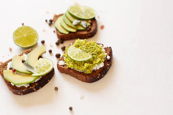 Sandwiches with avocado and cream cheese with grain bread. Sliced avocado on toast bread on white background, top view.