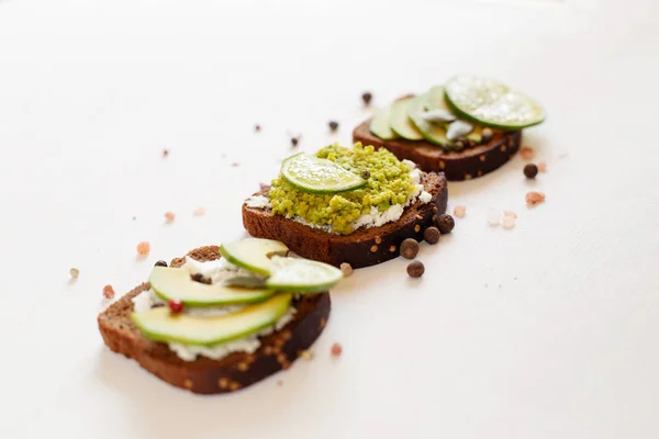 Sandwiches with avocado and cream cheese with grain bread. Sliced avocado on toast bread on white background, top view.