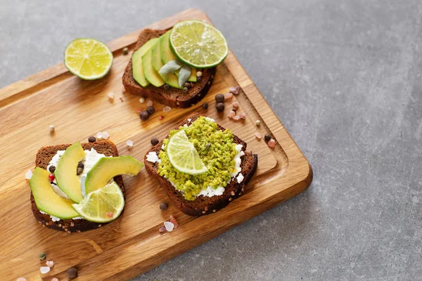 Sandwiches with avocado and cream cheese with grain bread. Sliced avocado on toast bread on wooden cutting board on grey background, top view.