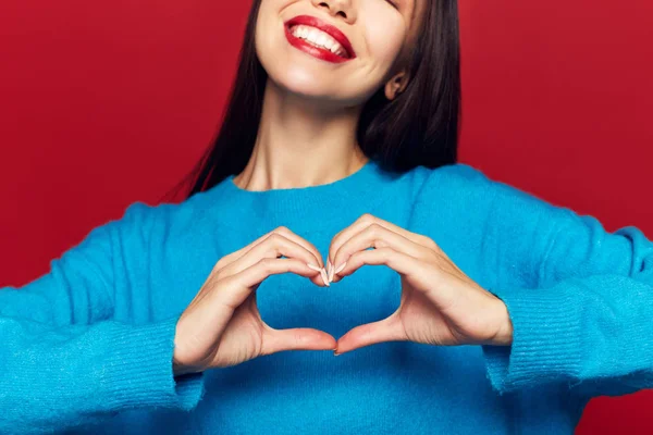 Woman making heart on chest over red background, studio shoot, valentine's day love concept.