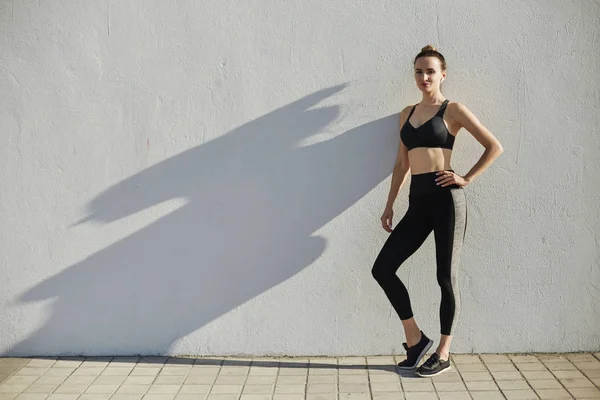 Fitness sporty woman with headphones relaxing after outdoor workout. Beautiful fit Girl in sport wear next to a wall. Weight Loss. Healthy lifestyle. Sporty healthy female, copy space.