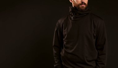 Siyah arka planda siyah eşofmanlı yüzü olmayan bir adam. Sakallı ve bıyıklı bir erkek model çerçevede rahatça duruyor..