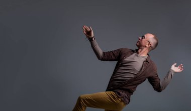 Örnek erkek testleri. Sürpriz ve sevinç hissi. Gri arka planda dans eden yetişkin bir adam. Moda fotoğrafçılığı