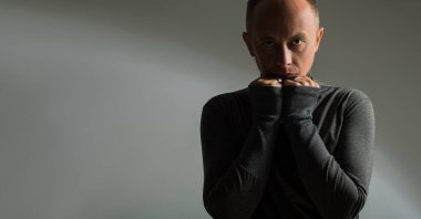 Erkek modeli, gri bir arkaplanda gradyanı olan testler yapıyor. Bir adam ellerini kendine bastırıyor ve özgüvenle kameraya bakıyor. Korku ve güç.