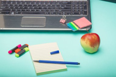 Laptop bilgisayar, kulaklık, defter, kalem, elma ve kahve kupası olan çalışma alanı. Düz konum, üst görünüm, turkuaz arkaplan