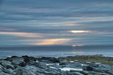 Maine kayalık sahil kapalı bulutlar arkasında yükselen güneş.