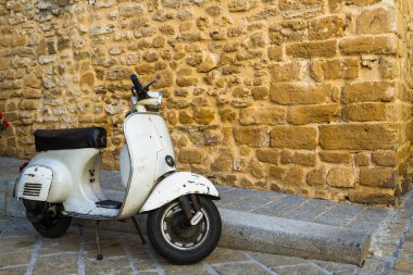 Altın rengi bir ancent taş duvarla önünde park etmiş bir beyaz, klasik Vespa scooter.