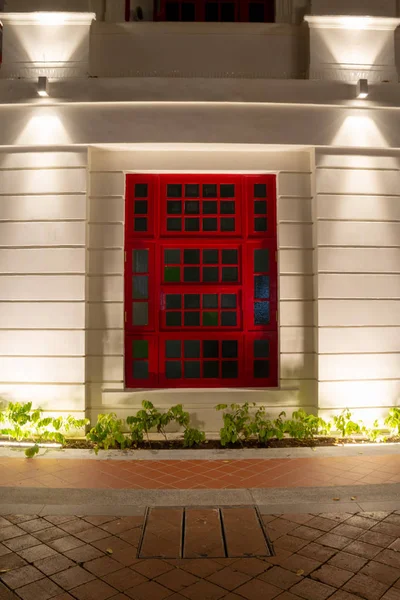 A red window frame on a white building at night.