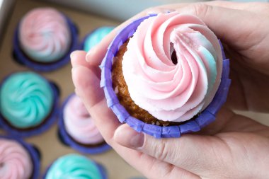 pembe ve mavi bir kutu cupcakes arka plan üzerinde bir kızın elinde krem ile Cupcake