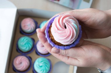 pembe ve mavi bir kutu cupcakes arka plan üzerinde bir kızın elinde krem ile Cupcake
