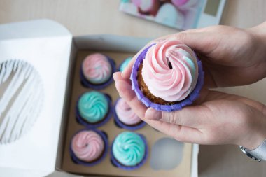 pembe ve mavi bir kutu cupcakes arka plan üzerinde bir kızın elinde krem ile Cupcake