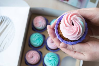 pembe ve mavi bir kutu cupcakes arka plan üzerinde bir kızın elinde krem ile Cupcake